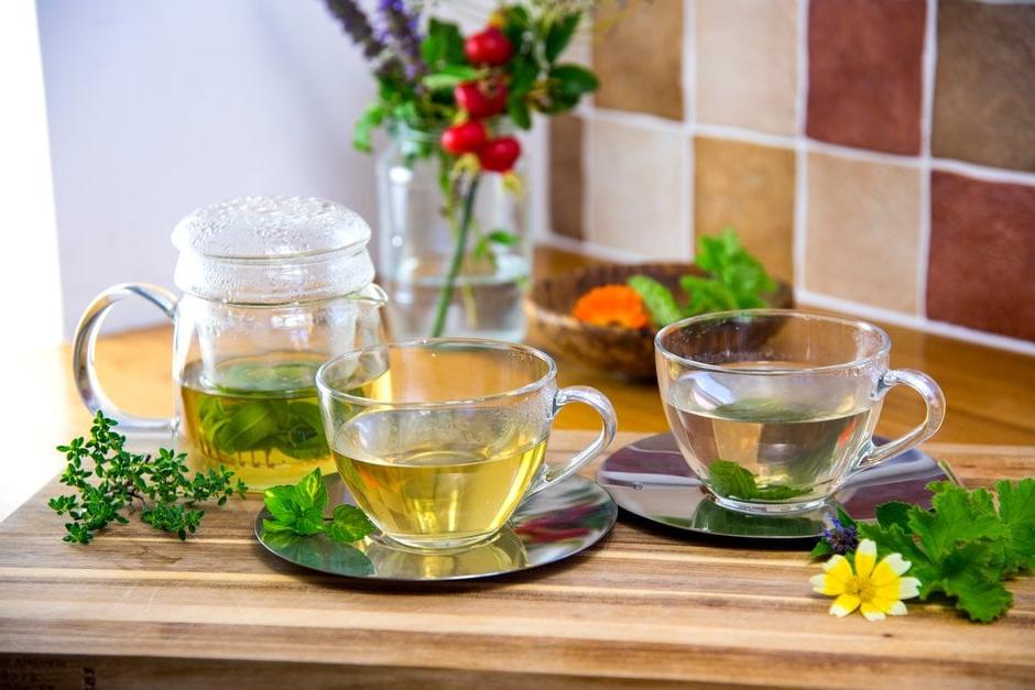 A pot of fresh mint leaf tea with two cups and a jar of botanicals