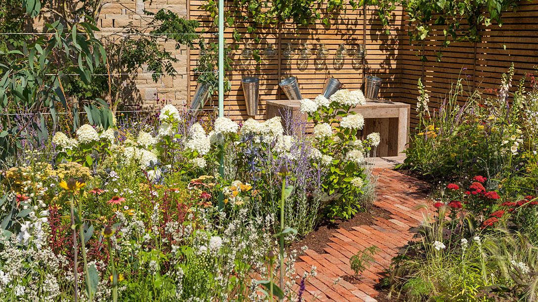 A mellow brick path leads to a stylish seating area where ivy cascades over slatted fencing.